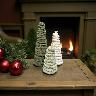 Three handmade chenille Christmas trees in cream, sage green, and dark forest green with textured finish, white star on medium tree, displayed on wood table with fireplace and red ornaments