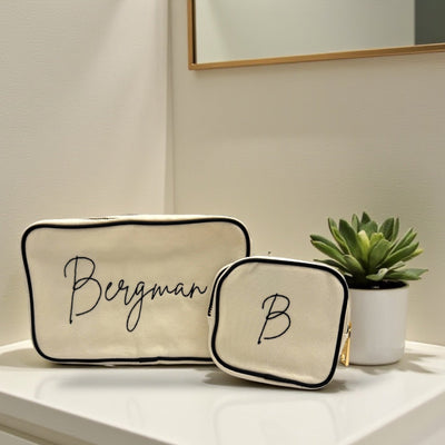 Two beige pouches with 'Bergman' and 'B' branding on a bathroom counter with a plant.